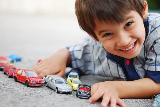 A little kid is laying and playing with cars
