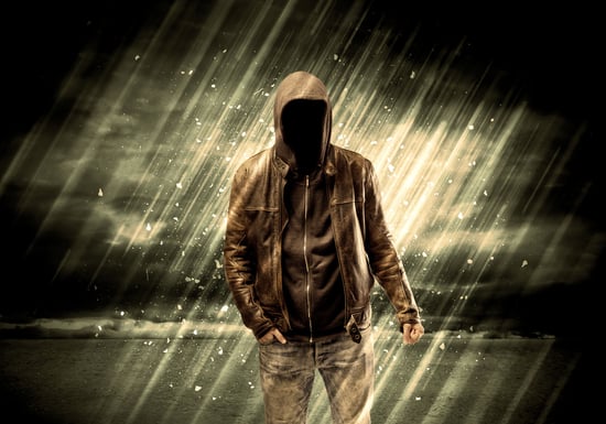 An incognito hooded stalker standing in the rain with his back in front of dark scary landscape concept