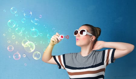 Pretty lady blowing big colorful bubbles on blue background