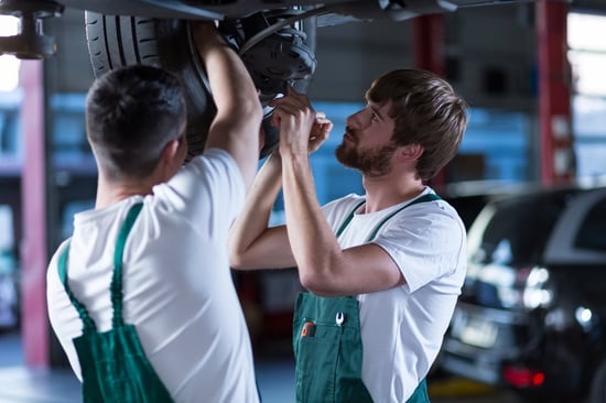 Young workshop employees working together underneath a lifted car