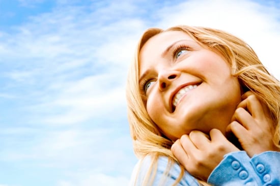 casual woman smiling outdoors with the sky in the background